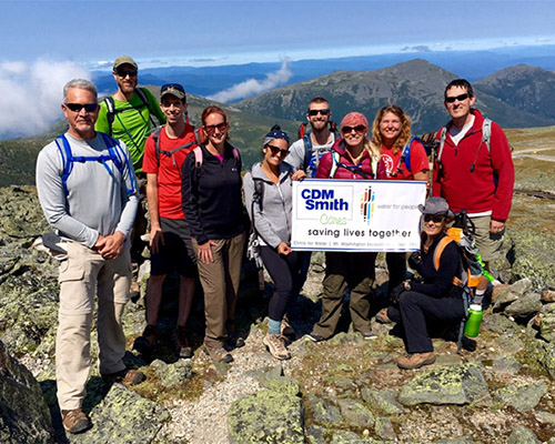 10 CDM Smith employees in hiking gear at the top of a mountain with a check for Water For People