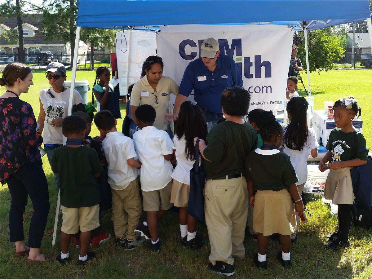 a group of kids standing around two CDM Smith employees under a tent at a Water Palooza event