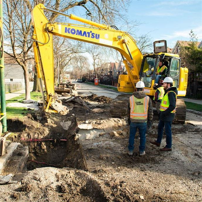 Two engineers standing next to evcavtor digging LSL holes in chicago street