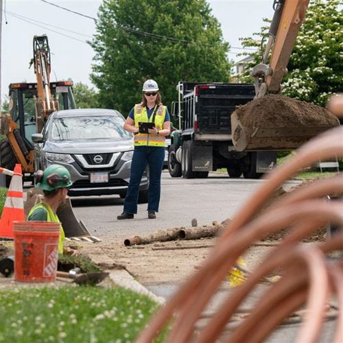 Lead Service Line Replacement construction with pipe and woman on ipad next to manhole