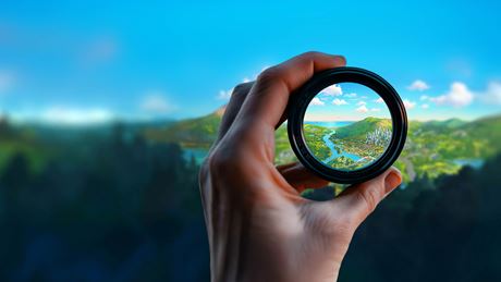 hand holding a magnifying glass looking through to a utopian landscape